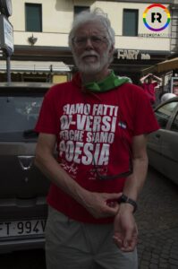 Una persona anziana con una maglia con scritto "Siamo fatti di-versi perché siamo poesia" e una spilletta ace